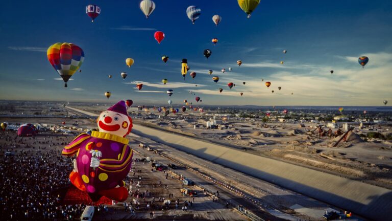 Dozens of colorful hot air balloons inflating and lifting off close together on the launch field at Albuquerque's Balloon Fiesta