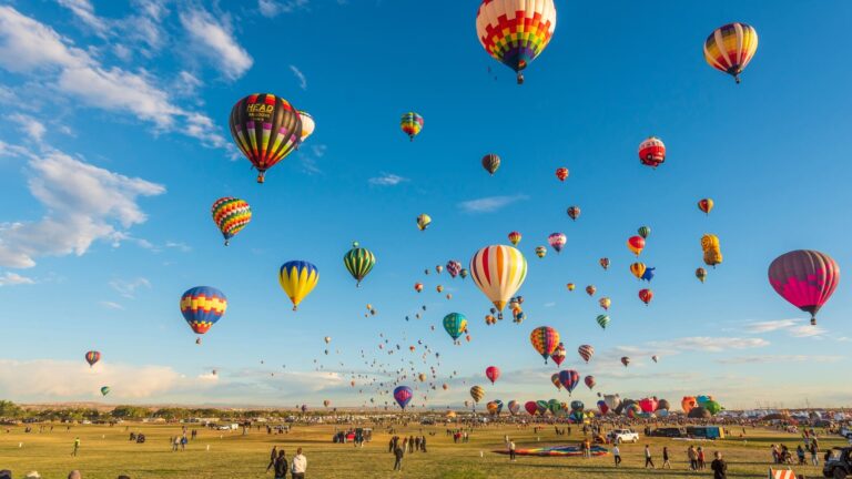 Aerial view of hundreds of hot air balloons rising above Albuquerque's outskirts near a flood control channel