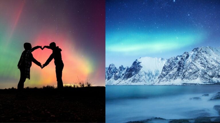 Travelers forming a heart beneath colorful northern lights beside snow-covered coastal mountains