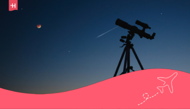 Telescope silhouetted against a twilight sky with a reddish moon and a bright streak overhead