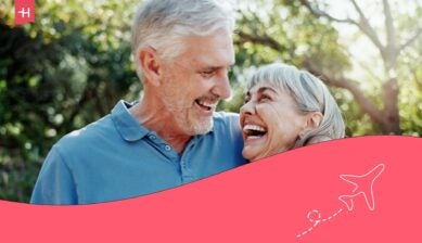 Smiling older couple enjoying time together outdoors in a sunny, leafy garden.