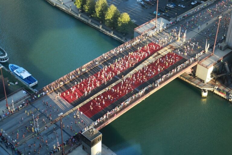 Aerial view of Chicago Marathon runners crossing a red-carpeted bridge over the Chicago River.