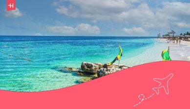 Tropical Jamaican beach with clear turquoise water, white sand, palm trees, and Jamaican flags along the shoreline.