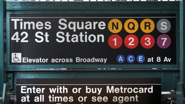 42nd Street subway station beneath the illuminated billboards of Times Square in New York City.