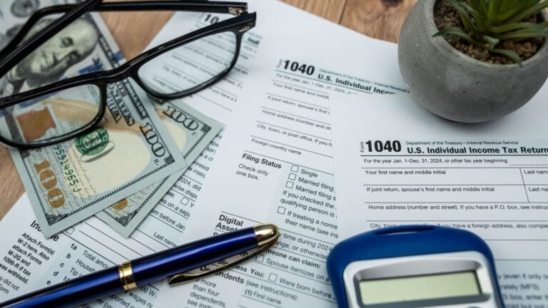 US dollar bills, an IRS Form 1040, reading glasses, and a calculator arranged for filing 2026 taxes
