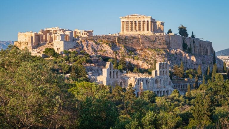 The Acropolis on its rocky hill in Athens, seen from Philopappos Hill in warm evening light under a clear sky.