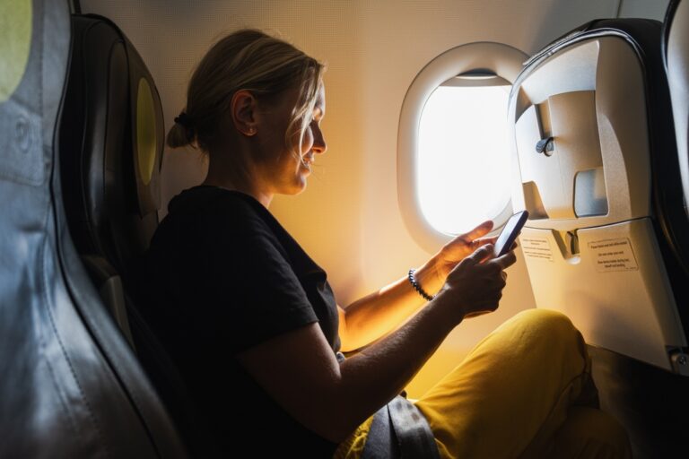 Woman using her smartphone while seated beside an airplane window.