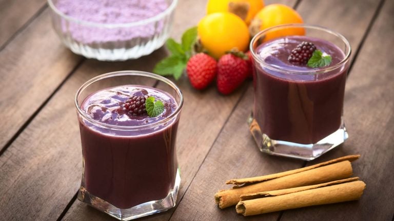 Glasses of thick, deep purple colada morada topped with fresh blackberries, with the front glass in sharp focus