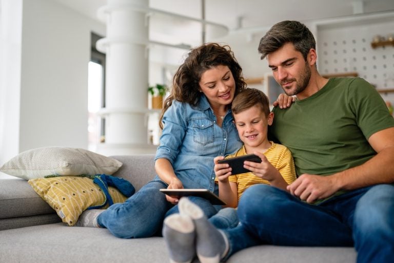 Two adults and a child sitting on a sofa, looking at a smartphone together.