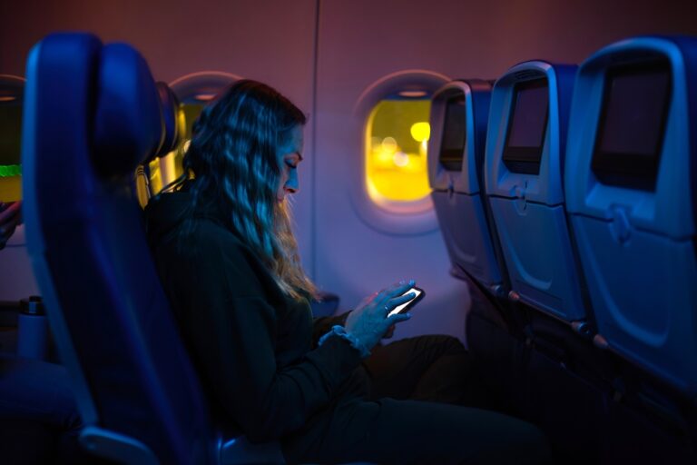 Woman using her smartphone in a dimly lit airplane cabin.