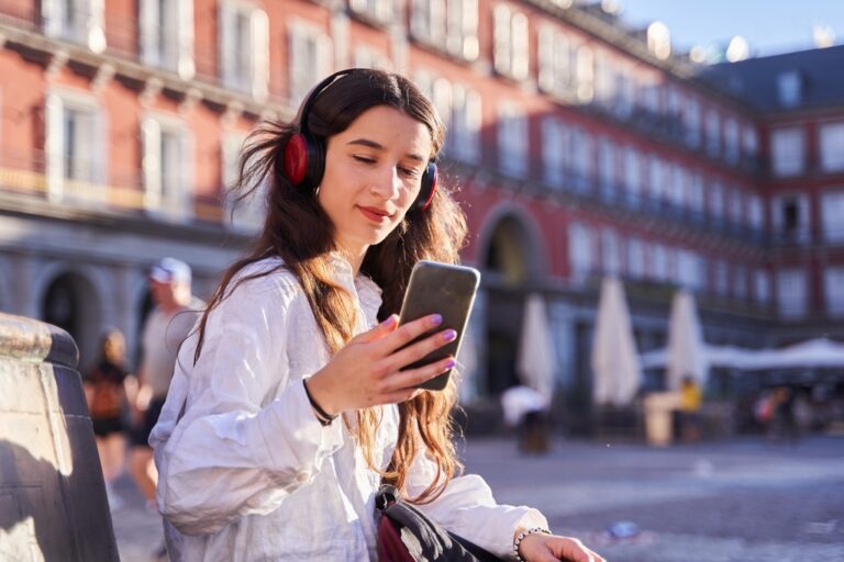 Woman wearing headphones and using a smartphone in a city square.