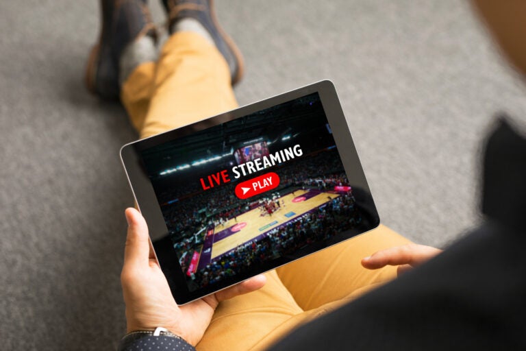 Person holding a tablet displaying a basketball live stream and play button.