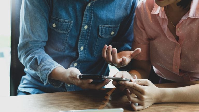 Two people holding smartphones side by side at a wooden table.