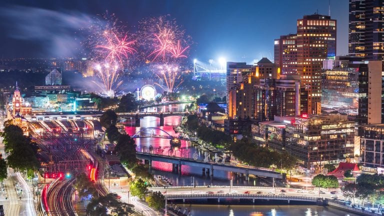 Colorful fireworks bursting in the night sky above the Yarra River, with Melbourne’s illuminated city skyline reflected in the water.
