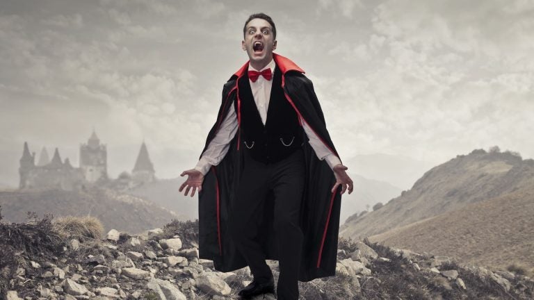 A man dressed as the vampire Count Dracula in a dark cape, standing in front of a castle