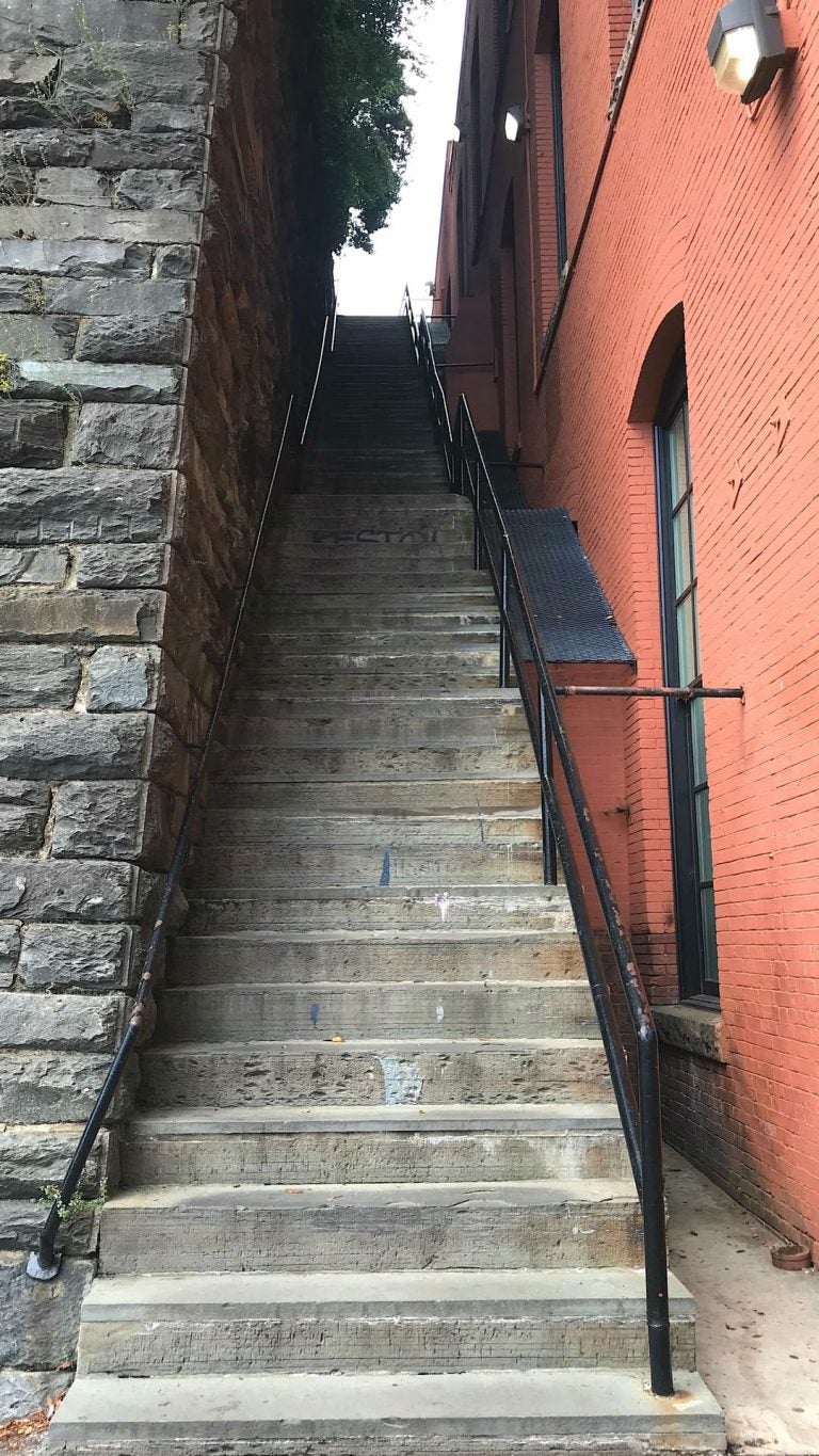 Steep, narrow stone staircase known as the Exorcist Steps, flanked by a stone wall and brick building in Georgetown, Washington, DC