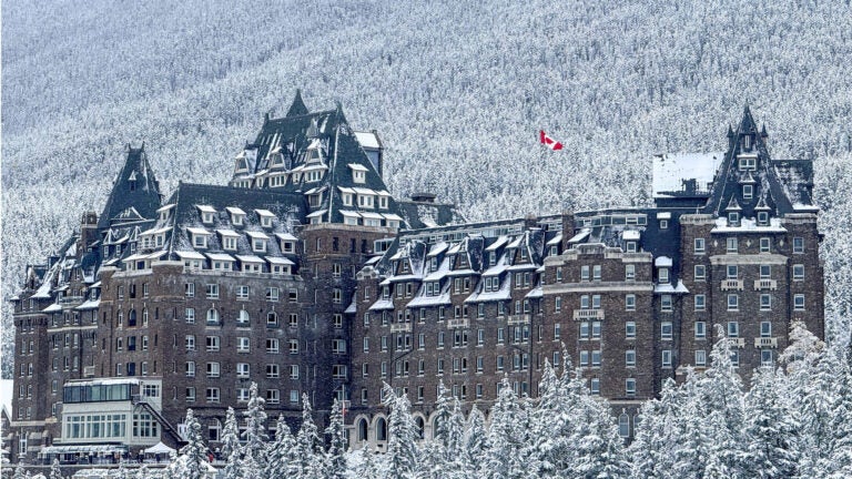 Stone exterior of Fairmont Banff Springs with green roofs covered in snow, surrounded by snowy pine forest in Alberta, Canada.