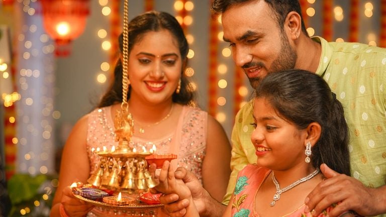 An Indian family lighting diya lamps together at home during Diwali