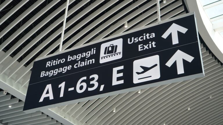 Overhead signs at Rome Fiumicino Airport pointing to baggage claim and the exit, labeled in Italian and English with a luggage icon.