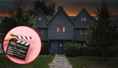 Salem’s historic Witch House with dark clapboard siding, steep triple gables, and glowing diamond-pane windows under an orange dusk sky, paired with a hand holding a film clapperboard in a circular inset