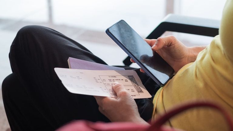 Traveler holding a passport and boarding pass while checking a smartphone