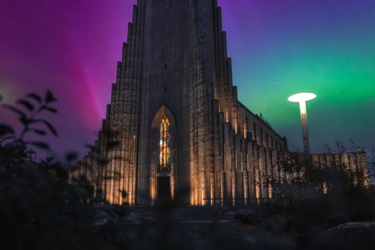 Hallgrimskirkja church rises over downtown Reykjavik with northern lights.