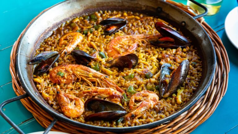 A wide iron paella pan filled with golden saffron rice, topped with whole shrimp, mussels and lemon wedges.