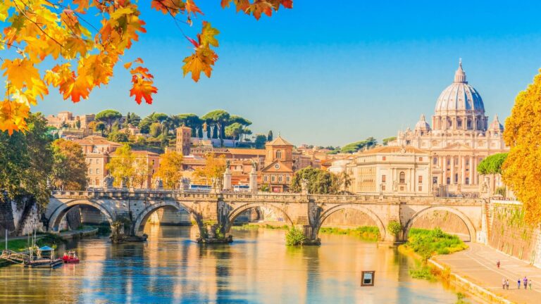The dome of St. Peter’s Basilica rising behind a stone bridge over the Tiber River in Rome on a clear autumn day.