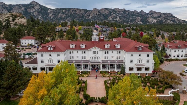 Aerial view of the white Stanley Hotel and its surrounding cabins in Estes Park, Colorado, framed by autumn trees and mountains.