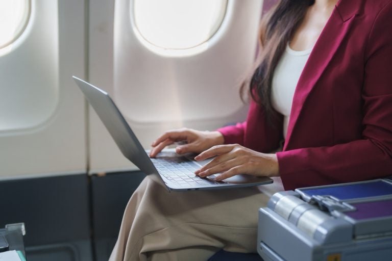 Woman using a laptop beside an airplane window.