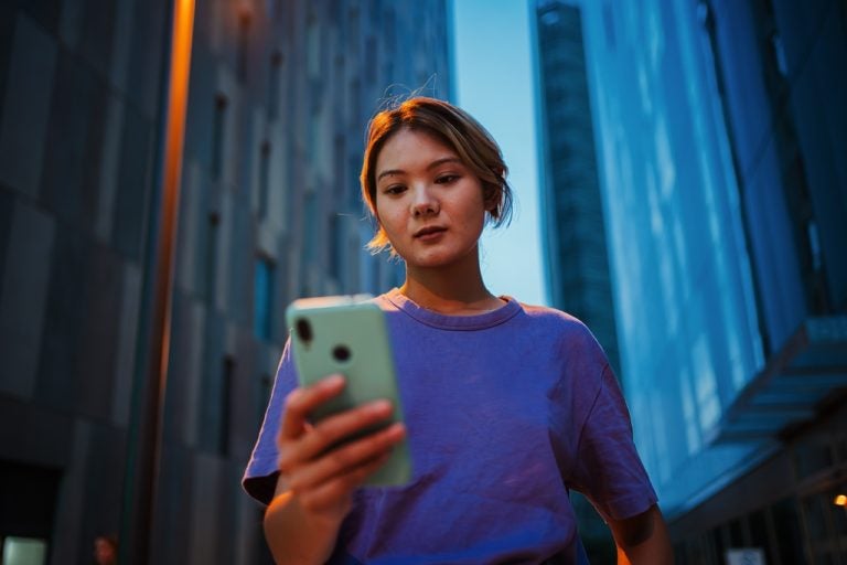 Woman looking at her smartphone while standing between city buildings.