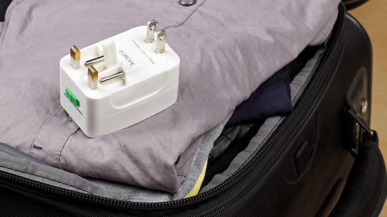 A travel power adapter resting on clothes in a packed suitcase