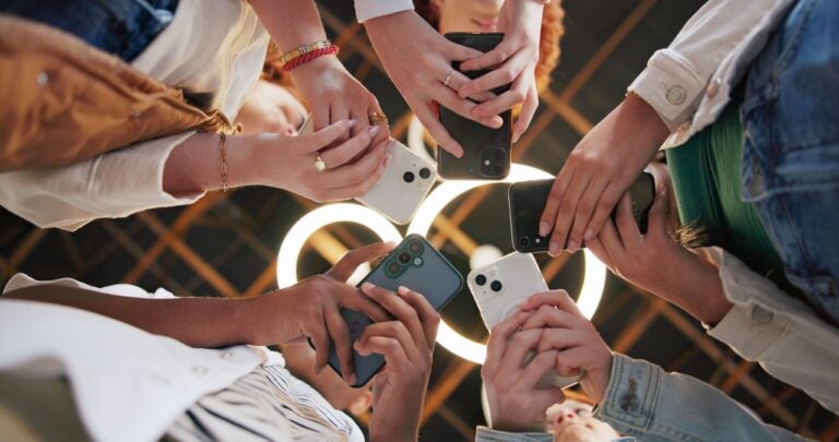 Group of friends holding smartphones together in a circle.