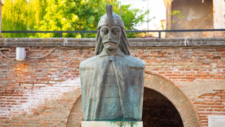 A stone bust of Vlad III, also known as Vlad the Impaler, with a mustache and a traditional cap, displayed at the Old Princely Court in Bucharest