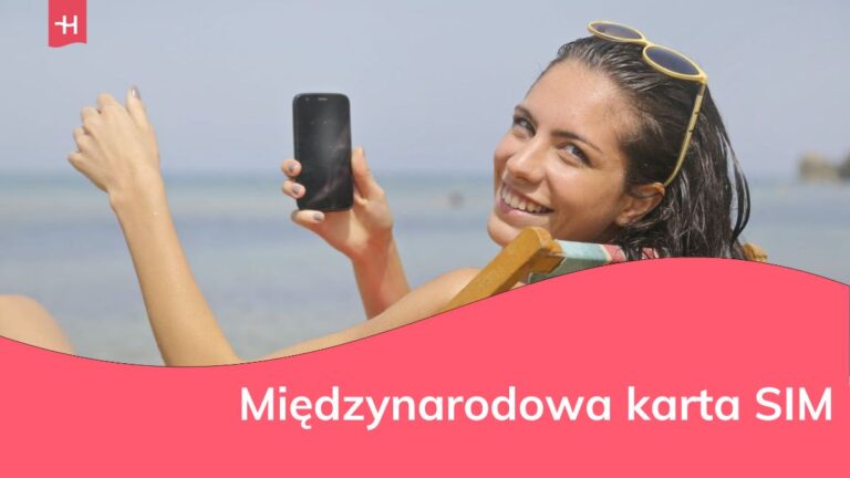 Uśmiechnięta kobieta trzyma w dłoni telefon siedząc na leżaku na plaży nad morzem.