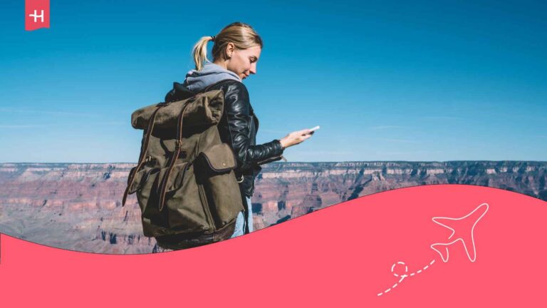 Eine junge Frau mit einem Rucksack, die vor dem Grand Canyon in den USA auf ihr Handy schaut