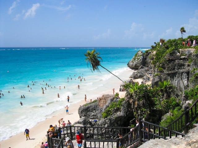 Leute auf Klippe mit Grasbäumen, die Leute am Meeresufer beim Schwimmen und Spazierengehen in Tulum, Mexiko beobachten