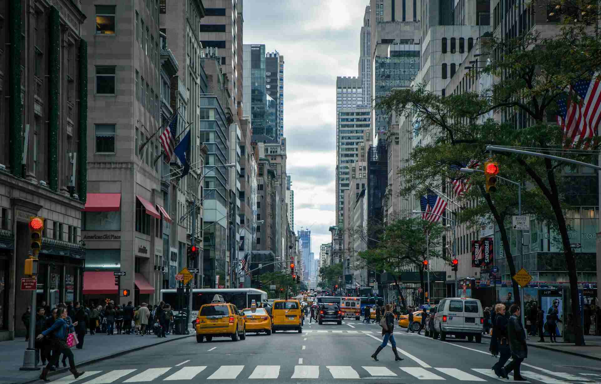 Eine typische Straße in New York, die braune Steingebäude, Wolkenkratzer und gelbe Taxis zeigt.