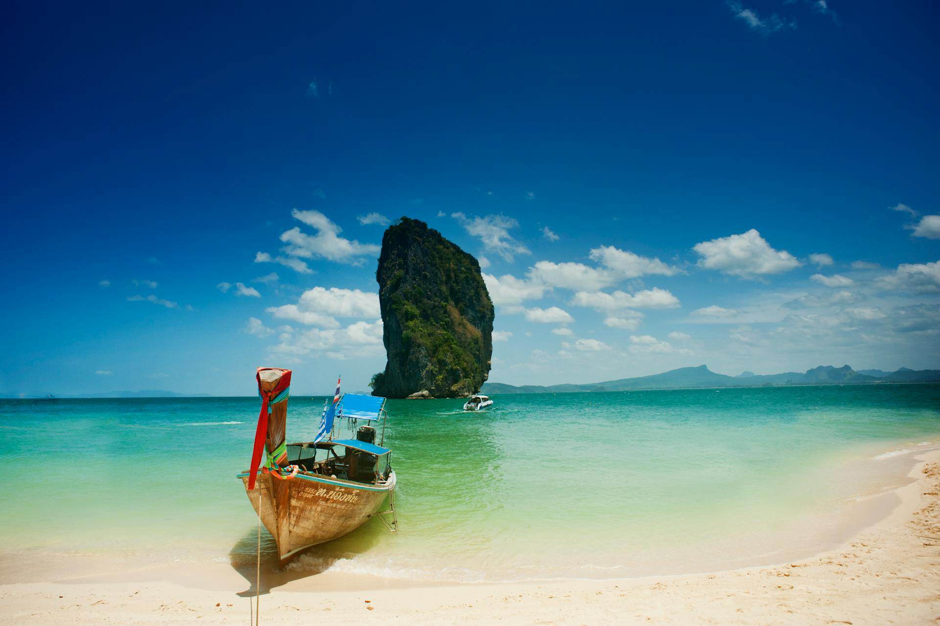 Ein buntes Holzboot an einem weißen Sandstrand mit türkisfarbenem Wasser in Thailand