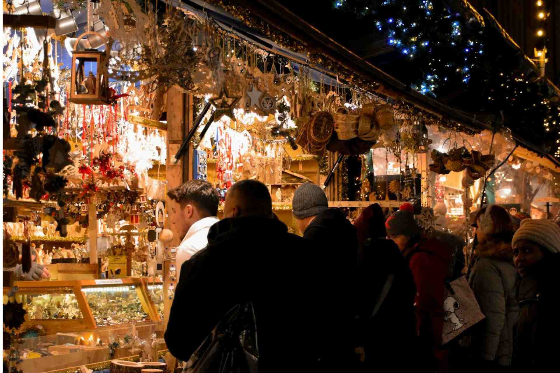 Leute vor einem beleuchteten Stand auf einem Weihnachtsmarkt in München, Deutschland