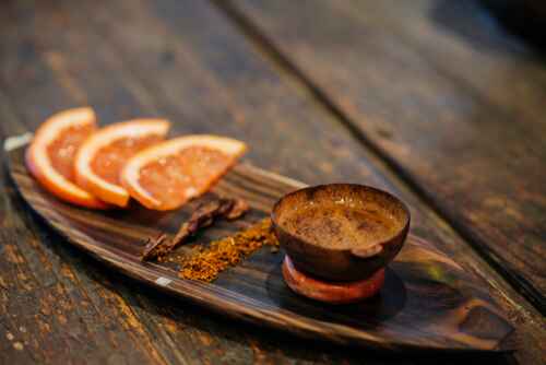 Mezcal, der in einer kleinen Holzschale serviert wird, die neben Orangenscheiben steht.