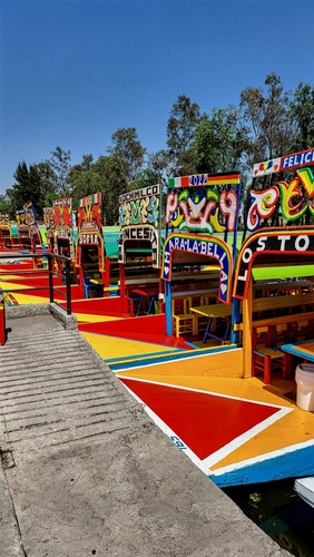 Eine lebhafte Szene mit traditionellen Booten aus Xochimilco, die wunderschön bemalt und entlang der Kanäle aufgereiht sind und die reiche Kultur und lebendige Atmosphäre dieses berühmten mexikanischen Reiseziels zeigen.
