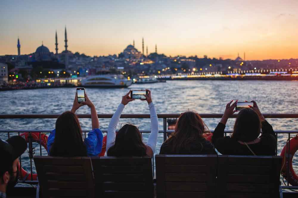 Des personnes sur un ferry en train de photographier la ligne d'horizon d'Istanbul au coucher du soleil.
