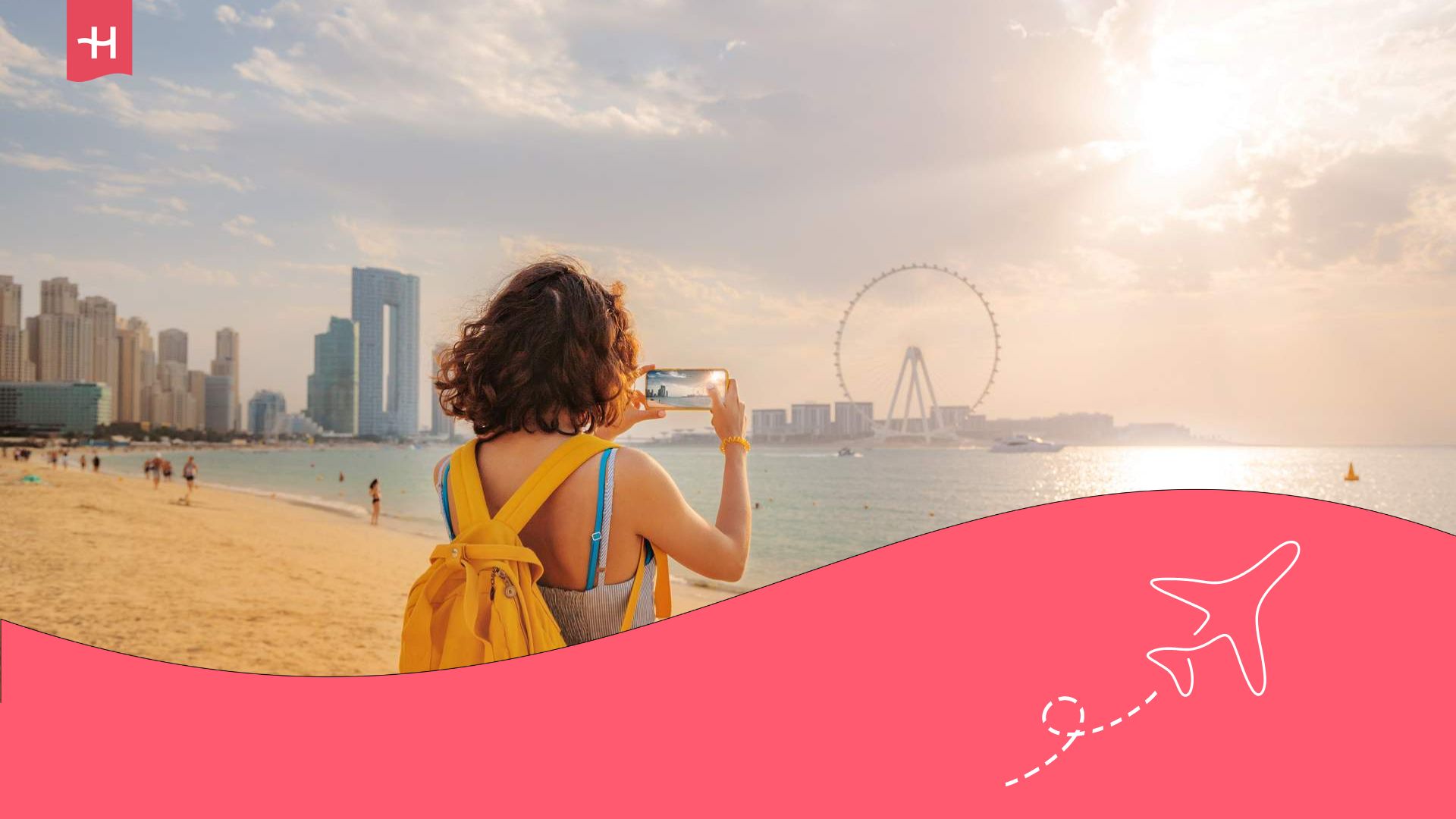 Eine junge Frau von hinten fotografiert die Wolkenkratzer Dubais vom Strand aus