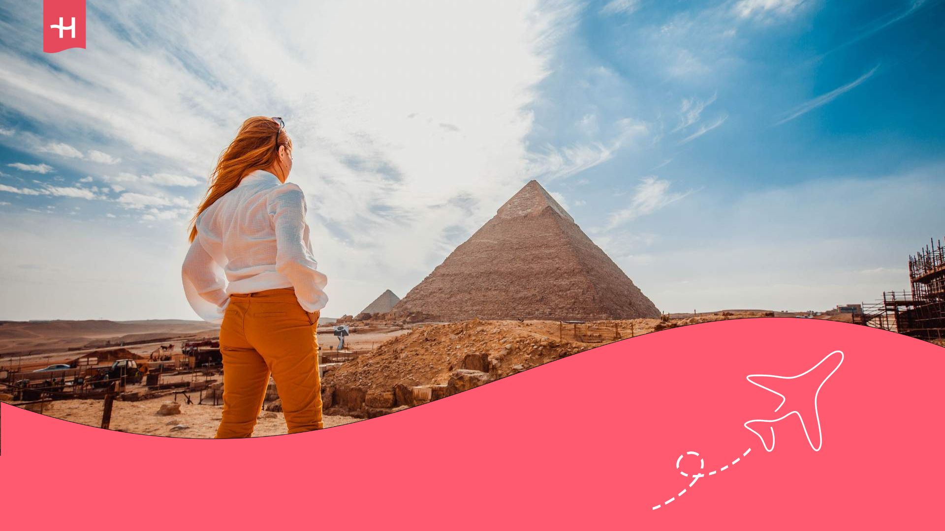 Eine junge Frau mit langen Haaren und von hinten betrachtet eine Pyramide in Ägypten.