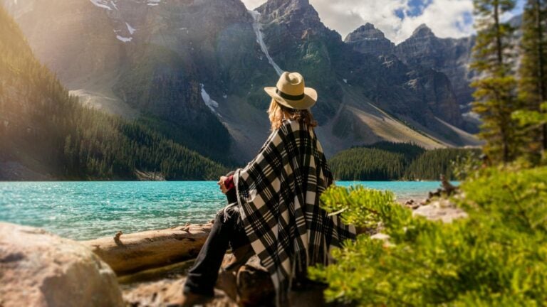 Frau sitzt an einem See der in eine Berglandschaft eingebettet ist.