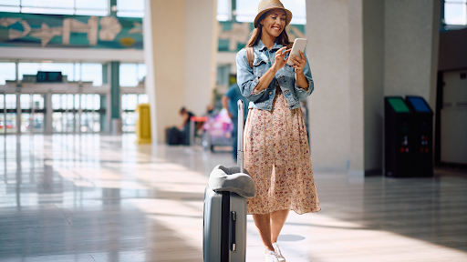 Eine Frau die am Flughafen auf ihr Handy blickt.