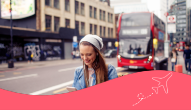 Eine junge Reisende in London, die auf ihr Handy schaut. Im Hintergrund ein roter Doppeldeckerbus.