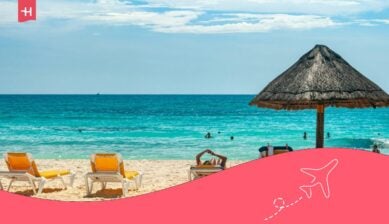 Sonniger Strand mit türkisblauem Meer, Liegestühlen und Strohdachschirm vor klarem Himmel.