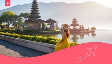 Frau im gelben Kleid mit Hut blickt auf einen balinesischen Wassertempel am See bei Sonnenaufgang.